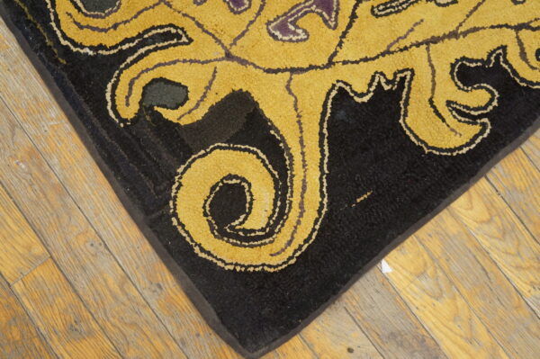 Textured black rug corner featuring bold, gold, scrolling patterns on light wood flooring.