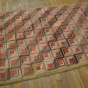Textured area rug featuring nested squares in red, tan, and brown, bordered by olive green on distressed wood flooring.