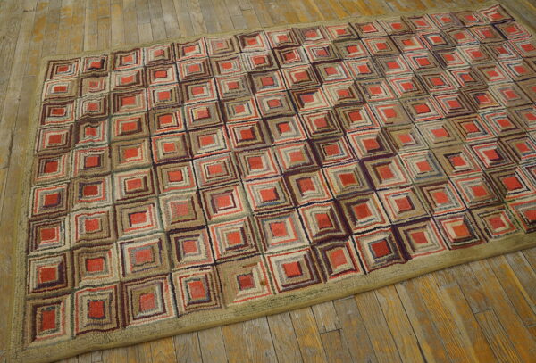 Textured area rug featuring nested squares in red, tan, and brown, bordered by olive green on distressed wood flooring.