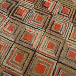 Textured rug displaying a geometric pattern of orange and multicolored concentric squares on wooden planks.