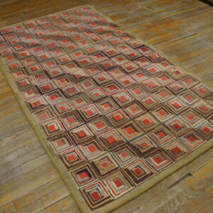 Low pile rug with red, brown, and beige concentric square patterns and a wide khaki border on wood floorboards.