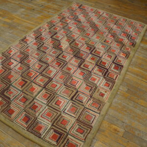 Textured low-pile rug with concentric red and multicolored squares and a khaki border on worn wood floors.