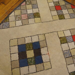 Beige rug with a quilt-like pattern of small colorful squares bordered by solid tan strips on wood floor.