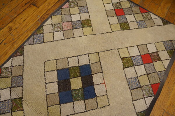 Beige rug with a quilt-like pattern of small colorful squares bordered by solid tan strips on wood floor.