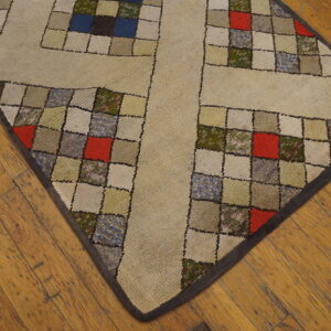 A beige rug with a multicolored patchwork grid pattern sits on warm, rustic wood floors.