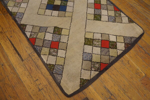 A beige rug with a multicolored patchwork grid pattern sits on warm, rustic wood floors.
