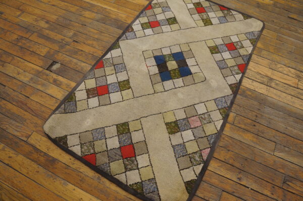 Beige low-pile rug with a multicolored patchwork square grid sits on distressed hardwood floor.