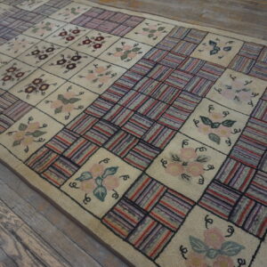 Cream checkerboard rug with floral designs and textured multicolored stripe squares, laid on weathered wood planks.