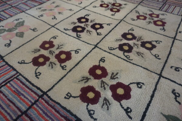 Looped cream rug with a black grid pattern, featuring maroon and pink flowers and a colorful striped border.