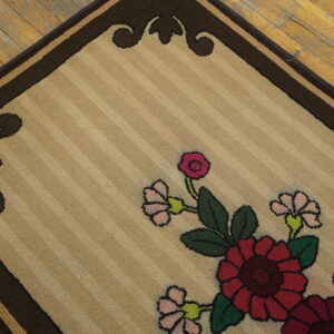 Beige looped rug with red, pink, and green floral design and a dark brown border on wood flooring.