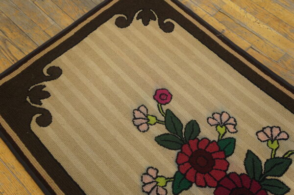 Beige looped rug with red, pink, and green floral design and a dark brown border on wood flooring.