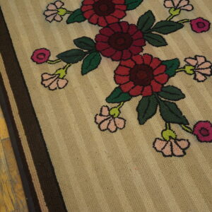Textured beige rug featuring large red, pink, and green floral motifs and striped borders on distressed wood flooring.
