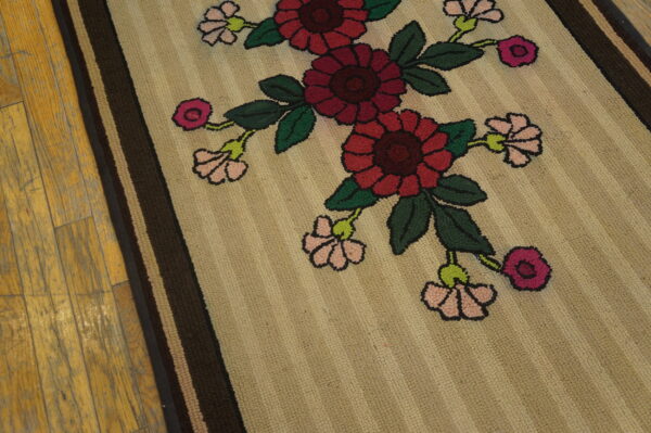 Textured beige rug featuring large red, pink, and green floral motifs and striped borders on distressed wood flooring.