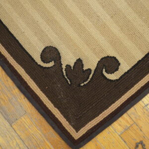 Tan and brown striped rug corner with a thick scroll border resting on yellow-toned plank flooring.