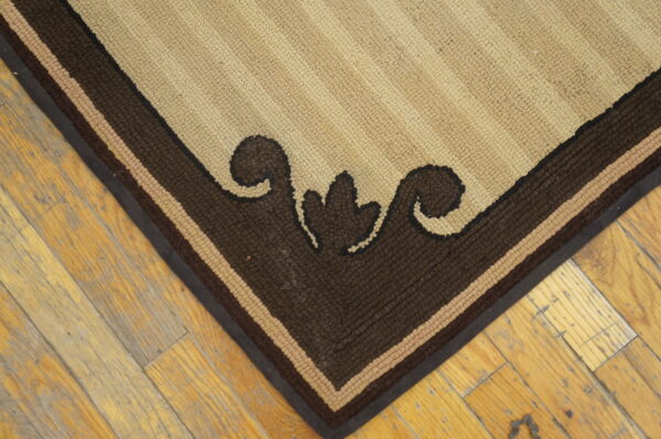 Tan and brown striped rug corner with a thick scroll border resting on yellow-toned plank flooring.