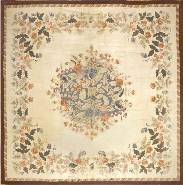 Ivory rug featuring a central blue floral bouquet and four corner sprays; it has striped and solid brown borders.