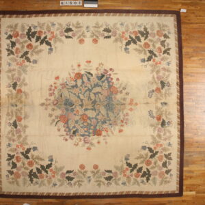 Square rug with a cream floral field, blue-gray central bouquet, and wide dark brown border on wood planks.