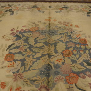 Textured area rug featuring a cream field and a dense central floral pattern in slate blue and warm tones.