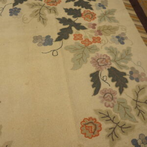 Tan rug with a dense multicolored floral and grape pattern bordering dark brown stripes on distressed wood floor.