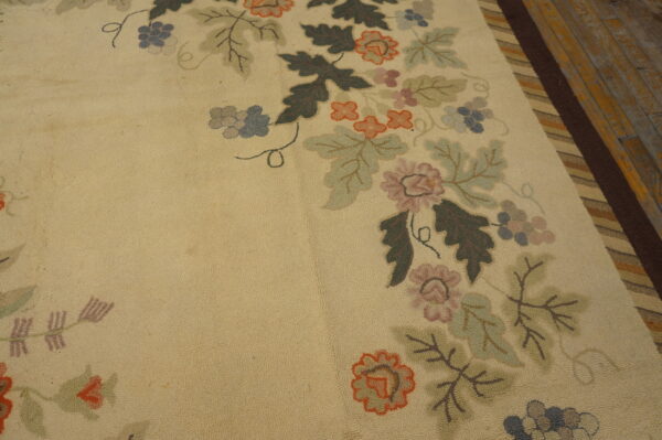 Tan rug with a dense multicolored floral and grape pattern bordering dark brown stripes on distressed wood floor.
