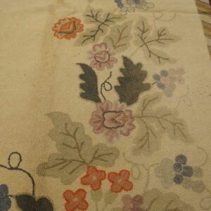 Cream looped rug with dusty rose, orange, and olive floral motifs next to a striped brown border on wood.
