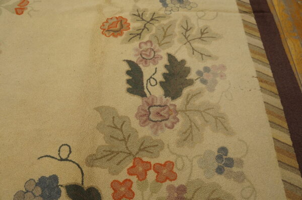 Cream looped rug with dusty rose, orange, and olive floral motifs next to a striped brown border on wood.