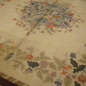 Cream rug with a dense floral and vine pattern in blue, coral, green, and purple, resting on wood floor.