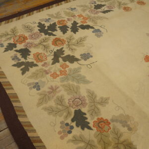 Low-pile rug with a cream field, a multicolored floral pattern, and a wide dark brown border on worn wood floor.