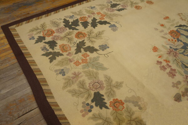 Low-pile rug with a cream field, a multicolored floral pattern, and a wide dark brown border on worn wood floor.