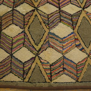 A highly textured rug featuring geometric diamond patterns in cream, olive, and multicolored stripes on wood flooring.