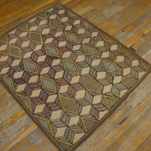 Medium pile rug with a colorful geometric cube pattern in cream and sage rests on worn hardwood flooring.