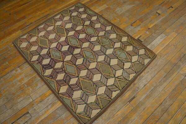 Medium pile rug with a colorful geometric cube pattern in cream and sage rests on worn hardwood flooring.