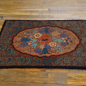 Textured loop pile rug with a central floral medallion in blues, browns, and reds on light wooden flooring.