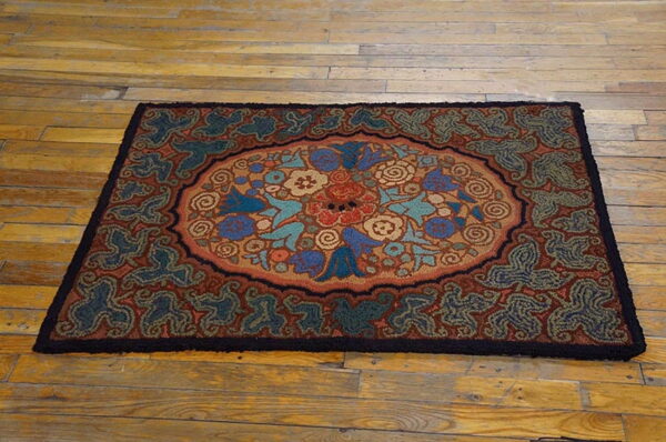 Textured loop pile rug with a central floral medallion in blues, browns, and reds on light wooden flooring.