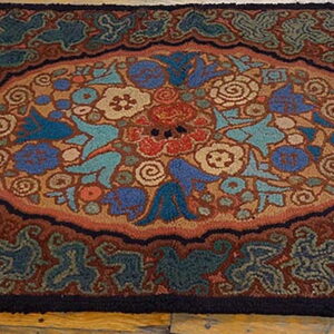Rustic hooked rug with blue, teal, and terracotta floral designs displayed on wood planks.