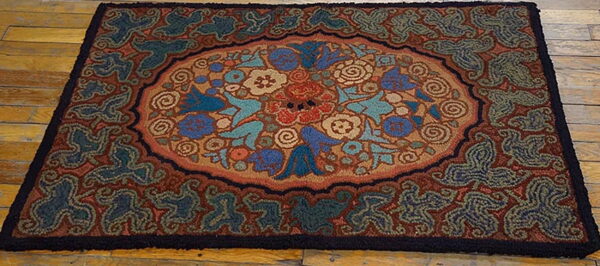 Rustic hooked rug with blue, teal, and terracotta floral designs displayed on wood planks.