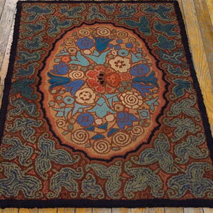 A coarse, hooked-style rug displaying an oval floral pattern in blue, red, and tan on rustic wood floors.
