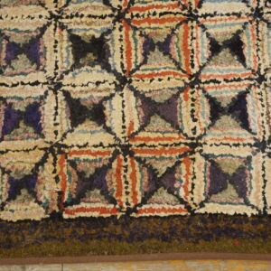 Shaggy rug corner showing a multicolored geometric pattern bordered by a solid dark olive edge on wood planks.