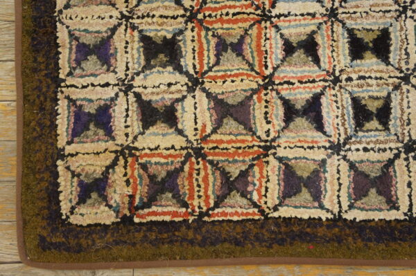 Shaggy rug corner showing a multicolored geometric pattern bordered by a solid dark olive edge on wood planks.