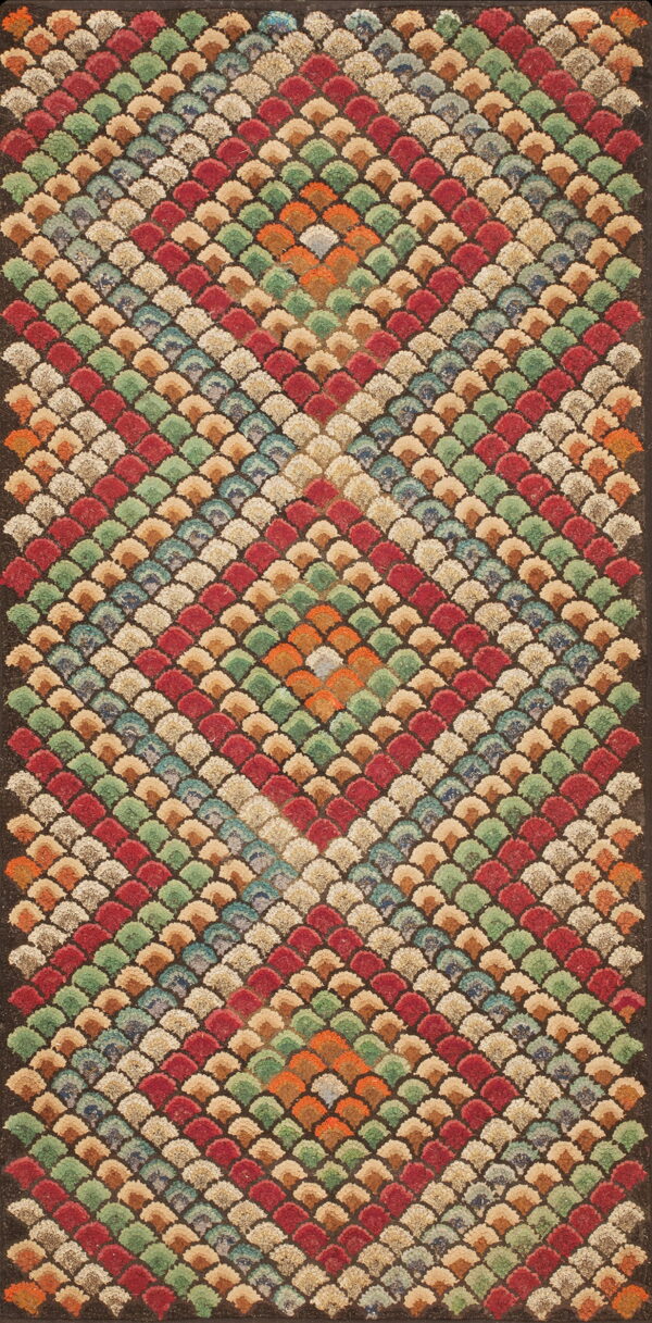 A textured, multicolored rug displaying repeating fan shapes in red, green, beige, and orange diamond motifs.