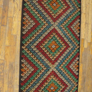 Textured runner rug with a repeating pattern of multicolored scalloped shapes on distressed yellow wood floors.