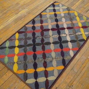 Multicolored hooked rug with repeating oval shapes on a gray ground, lying on diagonal wooden floor planks.