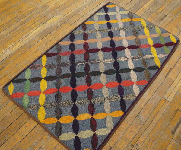 Multicolored hooked rug with repeating oval shapes on a gray ground, lying on diagonal wooden floor planks.