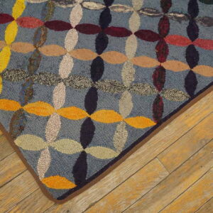 Multicolored hooked rug featuring blue, yellow, and red interlocking ovals on rustic wood plank flooring.