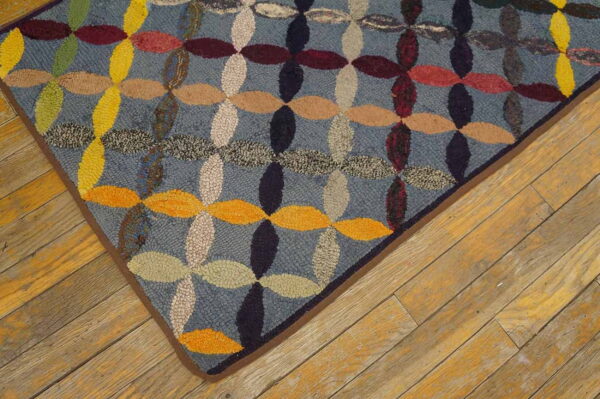 Multicolored hooked rug featuring blue, yellow, and red interlocking ovals on rustic wood plank flooring.