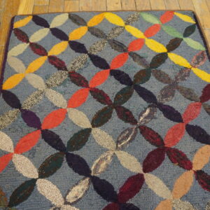 Textured blue rug featuring an interlocking multicolored oval pattern, visible on rustic wood flooring.