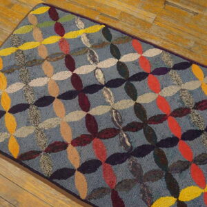 Hooked rug with an all-over multicolored ovals pattern on a blue-gray field over wood flooring.