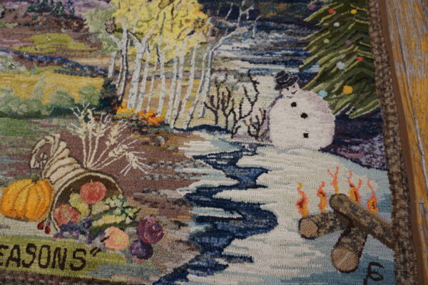High-pile multicolor rug with detailed seasonal scenes, including a snowman and cornucopia, beside wood flooring.