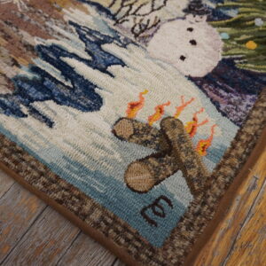 Textured, multi-colored hooked rug corner depicting a snowman, campfire, and winter scenery on rustic wood plank flooring.