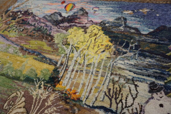 Textured multicolored rug depicting a detailed landscape scene with yellow trees, mountains, and hot air balloons.
